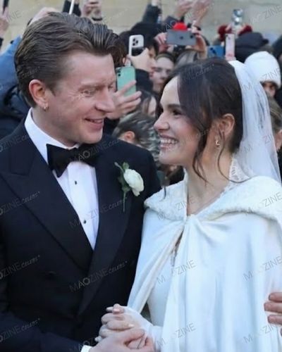 Close-up of Holly Ramsay in her hooded bridal cape smiling at husband Adam Peaty outside Bath Abbey after their wedding ceremony.