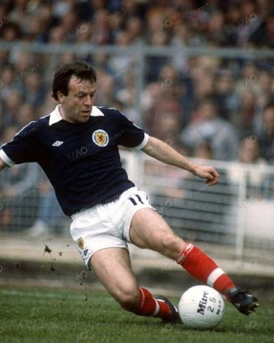John Robertson playing for Scotland in the blue national kit, seen sliding for the ball during an international match.