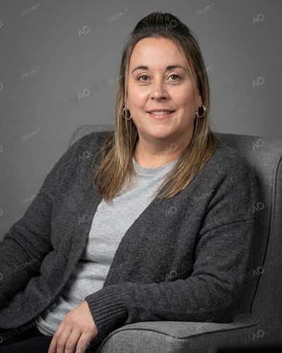 A professional portrait of Lisa Littler, mother of darts player Luke Littler, sitting in a grey armchair and smiling.