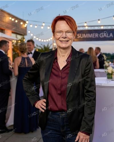 Rosemary Turner smiling at an outdoor Summer Gala event. She is wearing stylish glasses, a black blazer, and a maroon shirt, showcasing her elegant fashion sense.