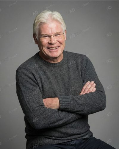 Portrait of John Playfair, retired fashion designer and husband of Prue Leith, smiling in a grey sweater.