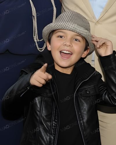 A close-up solo portrait of a young Jackson Chambers (son of Justin Chambers), smiling, pointing at the camera, and wearing a fedora hat.