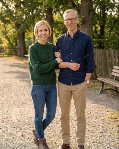 A rare candid photo of Mark Hines and Lucy Worsley standing in a park. Lucy is wearing a green sweater and Mark is in a blue shirt, both smiling and linking arms.
