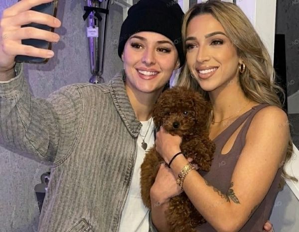 GK Barry and Ella Rutherford smiling in a mirror selfie holding their brown toy poodle dog Noodle.