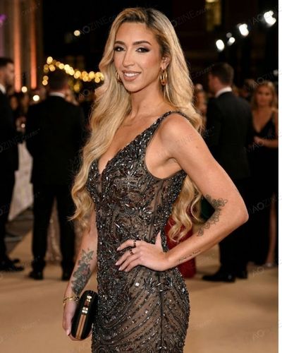 GK Barry (Grace Keeling) posing on the red carpet in a sparkling sheer black and gold gown.