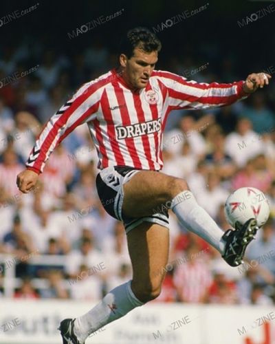 Neil Razor Ruddock kicking the football during a match for Southampton FC wearing red and white striped Drapers kit.
