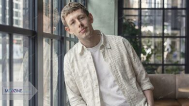 Josh Finan as Dan in BBC drama Waiting for the Out, wearing a striped shirt leaning against a window