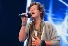 Harry Styles on X factor. He is holding a mic in his hand.